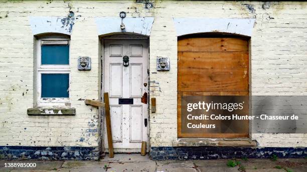 weathered brick facade with door and windows of an abandoned house and sidewalk in london - abandoned house stock pictures, royalty-free photos & images