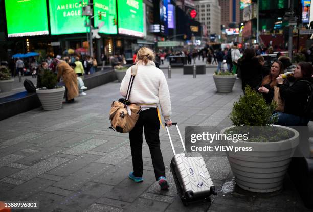 A Woman carries a suitcase by Times Square on March 31, 2022. In 2021 the city received just 32.9 million visitors, less than half the record total...