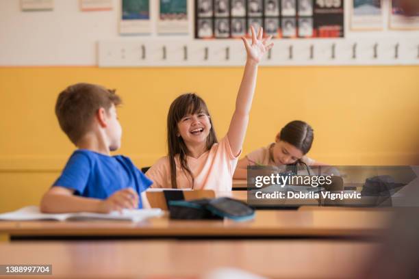 school girl raising hand in classroom and laughing - teachers pet stock pictures, royalty-free photos & images