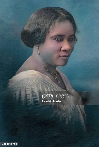 Colorized studio portrait of Madam C J Walker, wearing a fringe-trimmed dress and posing with her face turned toward the camera in...