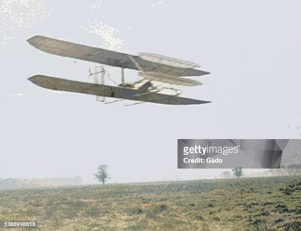 Colorized low-angle photograph depicting Orville and Wilbur Wright's early airplane, Wright Flyer II, gliding over Huffman Prairie in Dayton, Ohio,...