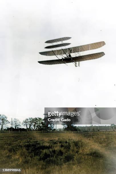 Colorized low-angle photograph depicting Orville and Wilbur Wright's early airplane, the Wright Flyer III, gliding over Huffman Prairie in Dayton,...