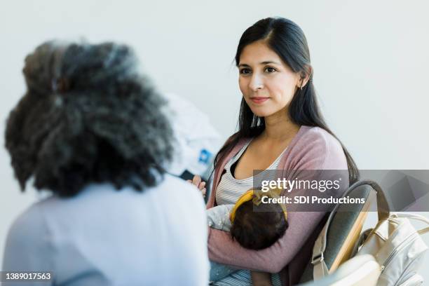schöne frau hält baby und hört auf unkenntliche person - wochenbettdepression stock-fotos und bilder