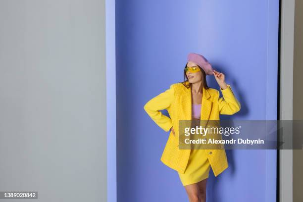happy fashion woman in bright yellow clothes posing in studio on blue wall with copy space. cheerful female model with beautiful smile - elegant woman smile stock-fotos und bilder