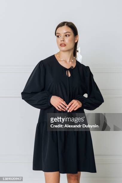 portrait of a beautiful model in a black dress posing in the studio on a white background in the room. woman new clothes catalog - traje negro fotografías e imágenes de stock