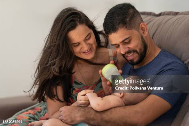 baby drinking milk from a bottle on daddy's lap - mum dad and baby stock pictures, royalty-free photos & images