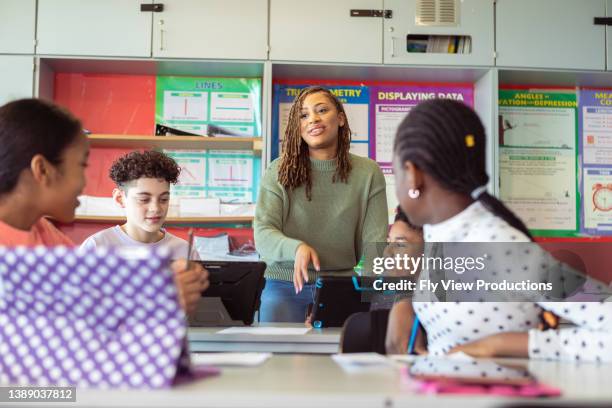 teacher answering questions as students work in class - teachers imagens e fotografias de stock