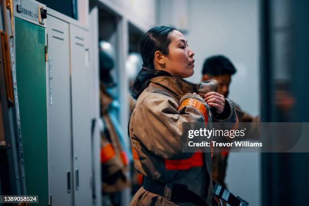 female firefighter putting on her protective equipment - firefighter foto e immagini stock