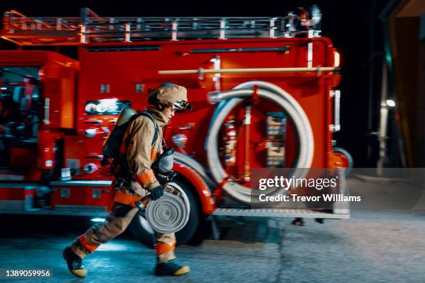 firefighter running with a hose next to a fire engine - brandweerwagen stockfoto's en -beelden