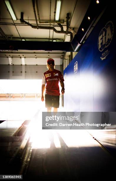 In very bright, lens flare inducing, back lit light, Spanish Scuderia Ferrari Formula One racing team racing driver Fernando Alonso walking in to the...