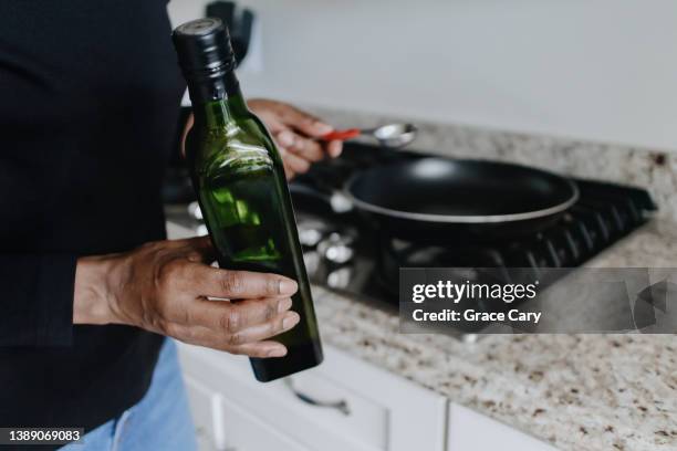 woman holds bottle of extra virgin olive oil to pour in frying pan - extra virgin olive oil stock pictures, royalty-free photos & images