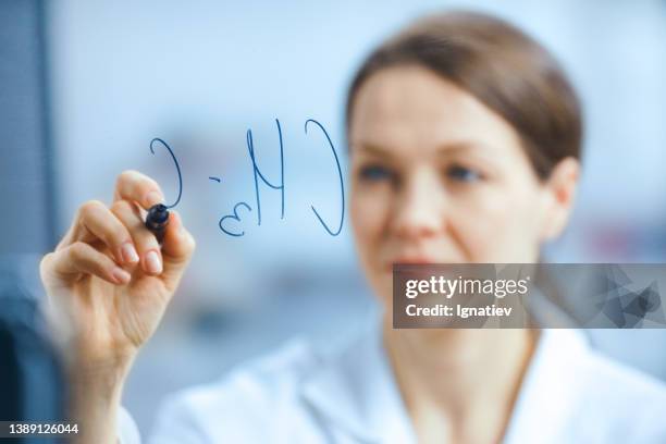 a defocused scientist in a white robe writes a chemical formula on a glass board with a marker - doctors script stock pictures, royalty-free photos & images