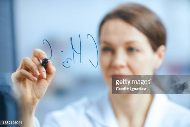 um cientista desfocado em um manto branco escreve uma fórmula química em uma tábua de vidro com um marcador - artigos de vidro de laboratório - fotografias e filmes do acervo