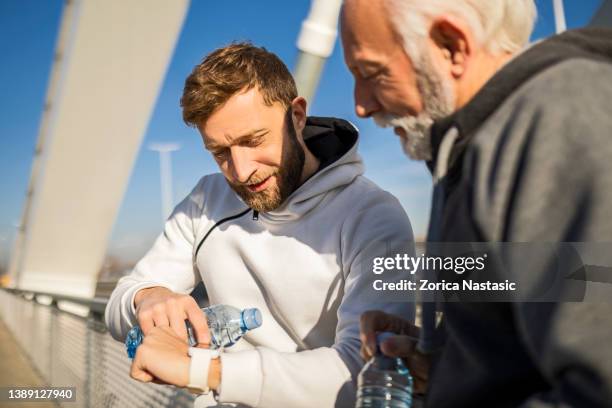 mature and young man jogging looking at smart watch - father sun stock pictures, royalty-free photos & images