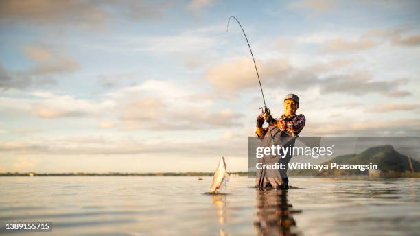 young man fishing on a lake at sunset and enjoying hobby - vangen stockfoto's en -beelden