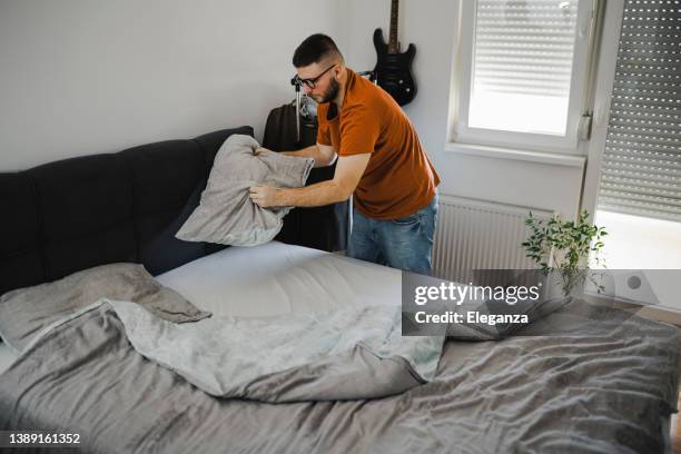 chef de maison faisant le lit et organisant la chambre le matin, tout en faisant le ménage - linge de lit photos et images de collection