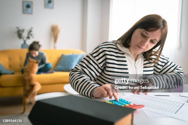 woman managing the monthly family budget while her daughter plays with a dog in the background. - femme facture photos et images de collection