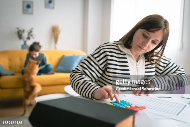 woman managing the monthly family budget while her daughter plays with a dog in the background. - budget bildbanksfoton och bilder