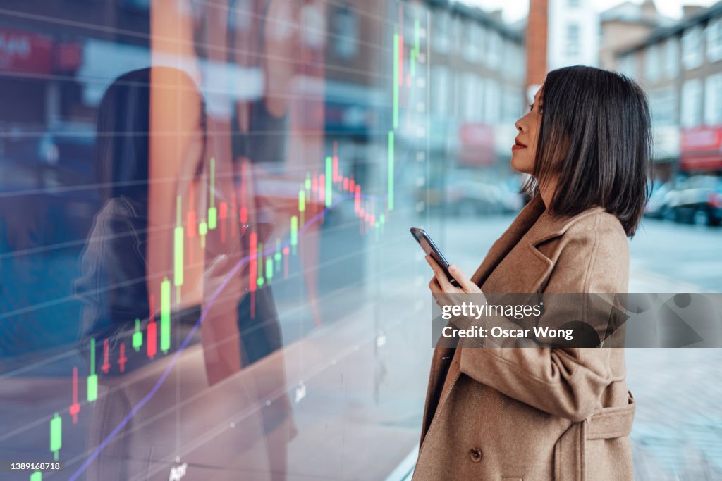 Young Asian businesswoman looking at stock exchange market trading board