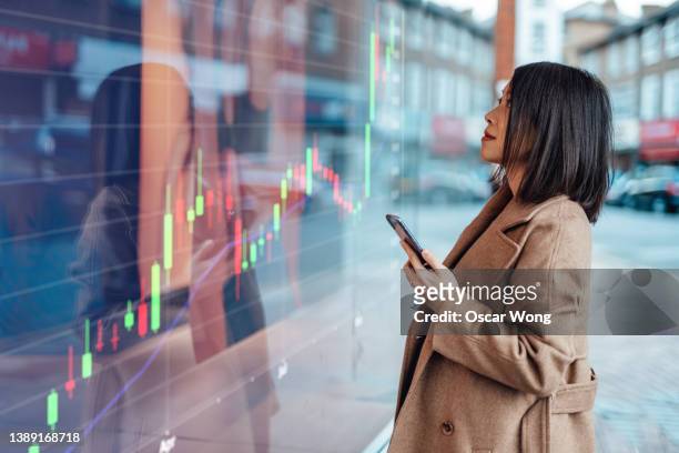 young asian businesswoman looking at stock exchange market trading board - valores imagens e fotografias de stock