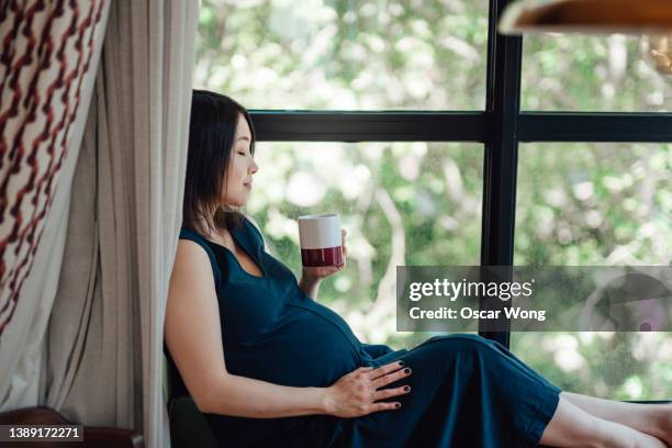 pregnant woman enjoying a cup of coffee while sitting by the window with lush green garden view - english tea room stock pictures, royalty-free photos & images