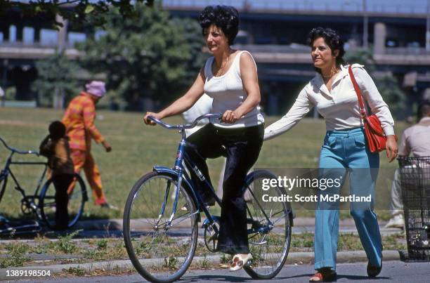 Steadied by her friend, an unidentified woman learns to ride a bicycle on a path in Flushing Meadows Park, in the Corona neighborhood of Queens, New...