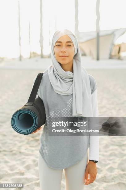 pretty portrait of muslim woman in hijab with black mat for morning yoga. beautiful sunlight - muslim woman beach stock pictures, royalty-free photos & images