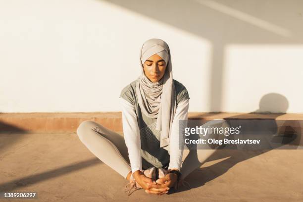 Muslim woman in hijab sitting and stretching legs on yoga practice, sportive and healthy lifestyle