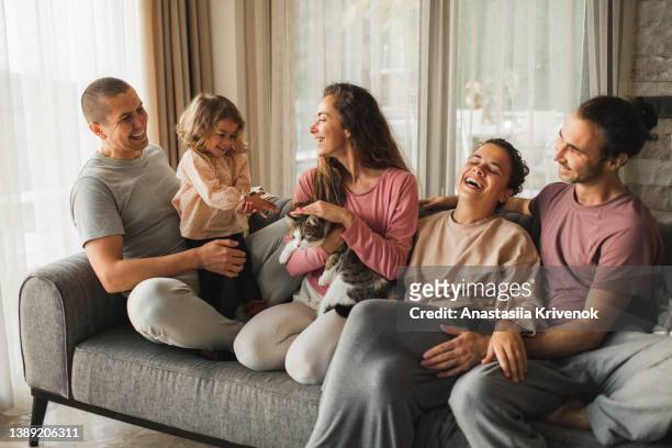 smiling family sitting on sofa with cat and little child and having fun. - onkel stock-fotos und bilder