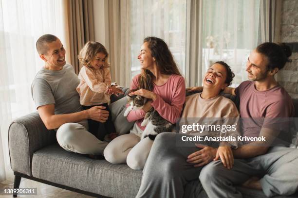 smiling family sitting on sofa with cat and little child and having fun. - uncle stock pictures, royalty-free photos & images