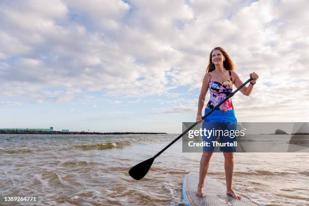 mature australian woman using stand up paddle board in the early morning - paddleboarding australia stock pictures, royalty-free photos & images