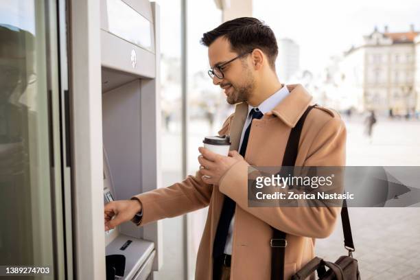businessman holding credit card at an atm - atm stock pictures, royalty-free photos & images