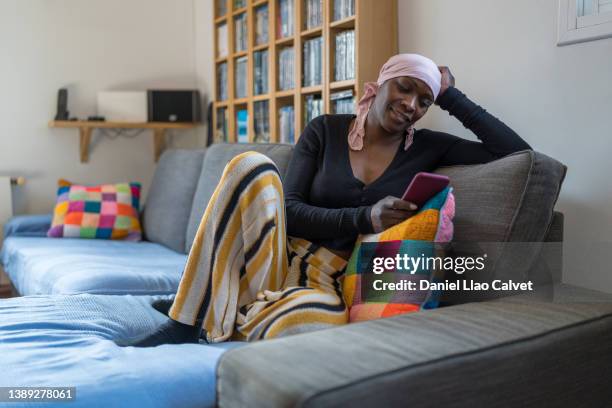 woman with cancer after radiation therapy at home reading text messages - headscarf home stockfoto's en -beelden