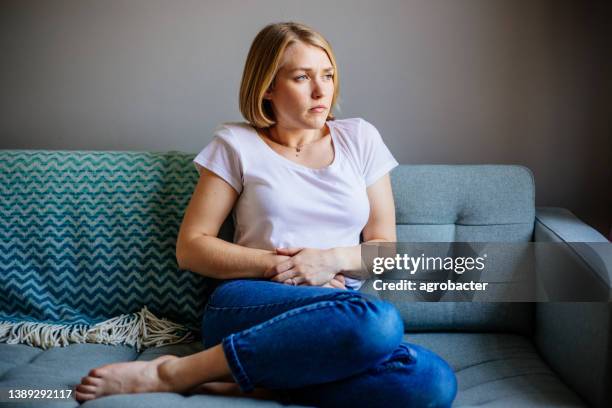 woman experiencing stomach pain while lying on the sofa at home - women pain stock pictures, royalty-free photos & images