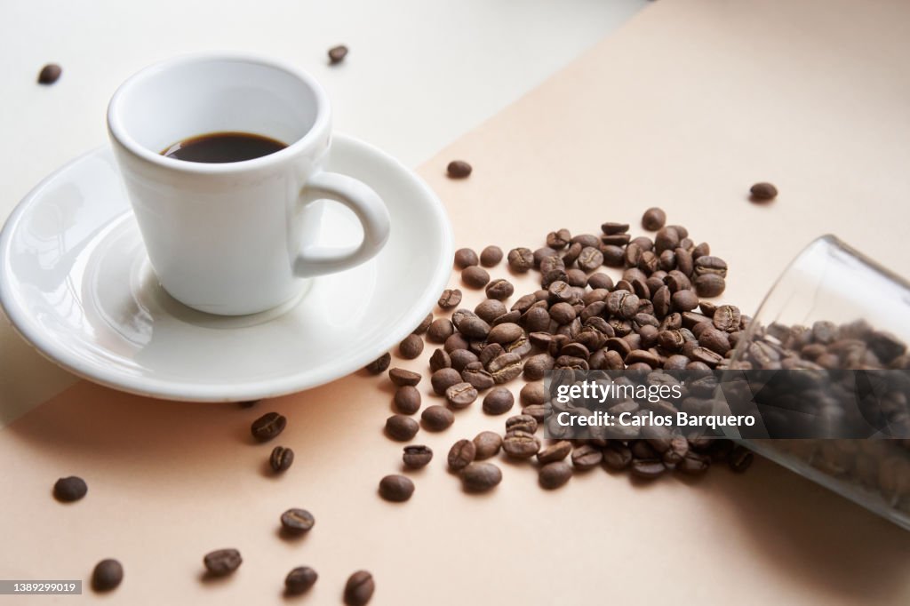 Close up photo of black coffee cup and dropped coffee beans.