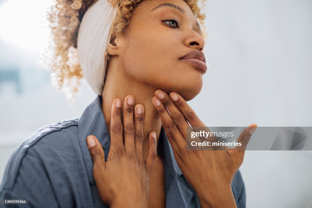 Mujer bonita que se aplica crema facial en el cuello