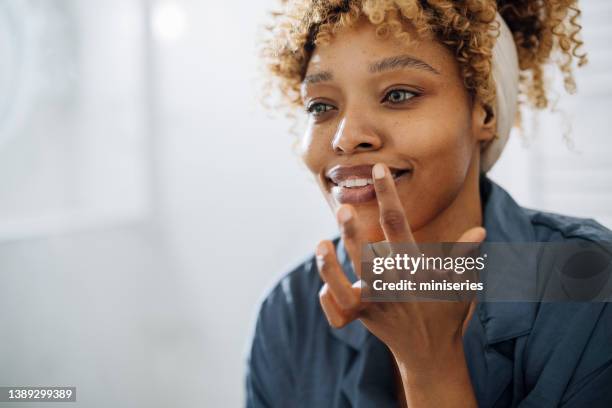 schöne grünäugige frau, die lippenbalsam auf ihre lippen legt - cream mouth stock-fotos und bilder