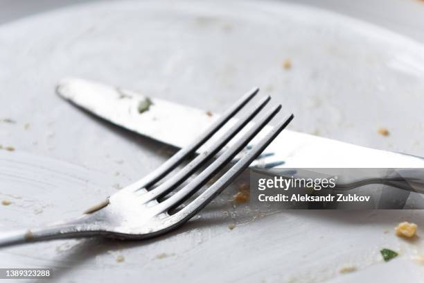 a dirty empty plate, fork and knife on a wooden table. used cutlery, symbolizing the end of lunch or dinner. - cleaning after party - fotografias e filmes do acervo