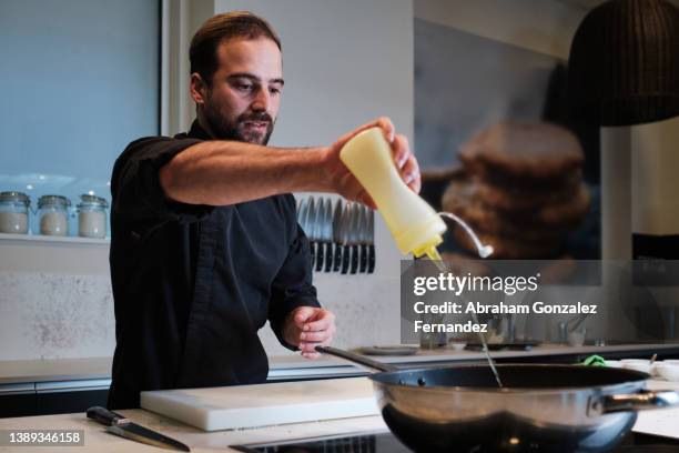 chef pouring oil on pan in modern kitchen - pouring sauce stock pictures, royalty-free photos & images