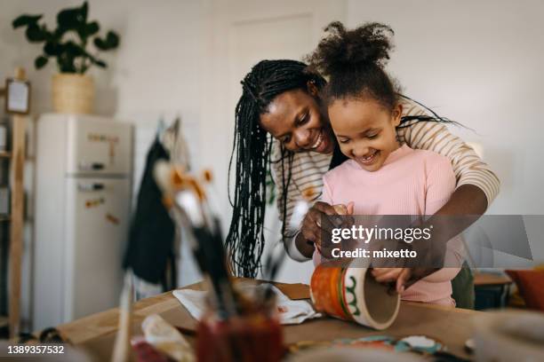 mother assisting daughter in painting flower pot at home - painting pottery stock pictures, royalty-free photos & images