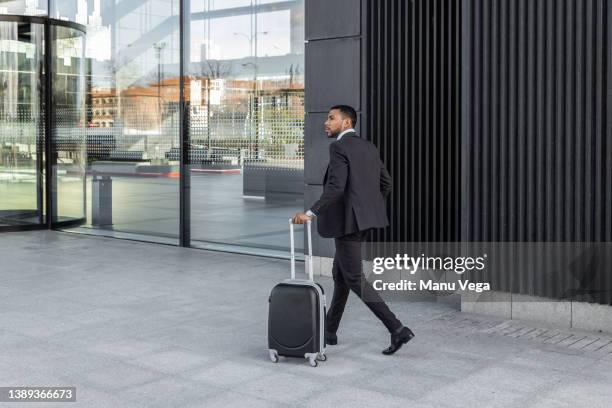 businessman walking with suitcase on wheels in city - rollkoffer stock-fotos und bilder