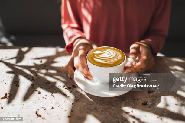 woman hands holding cup of fresh aroma cappuccino. unrecognizable person. cafe culture and lifestyle. - coffee art stockfoto's en -beelden