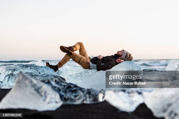 el hombre acostado en el hielo de cristal en la playa diamond en islandia - jokulsarlon lagoon fotografías e imágenes de stock