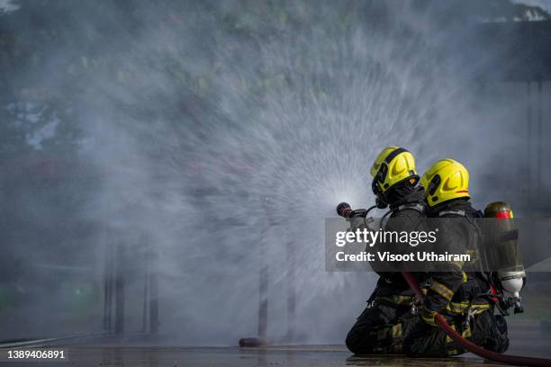 firefighters fighting fire during training,fire and rescue training school regularly to get ready,firefighter using extinguisher and spray water from hose for fire fighting. - emergency services equipment stock pictures, royalty-free photos & images