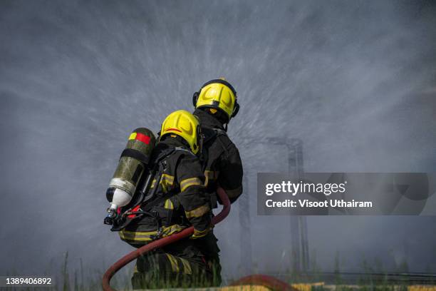 firefighter spraying high pressure water to fire,fireman using water and extinguisher to fighting with fire flame in an emergency situation. - brandslang stockfoto's en -beelden