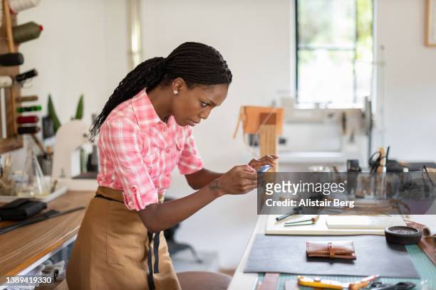 female artist photographing a product in her leatherwork studio - taking photo with phone stock-fotos und bilder