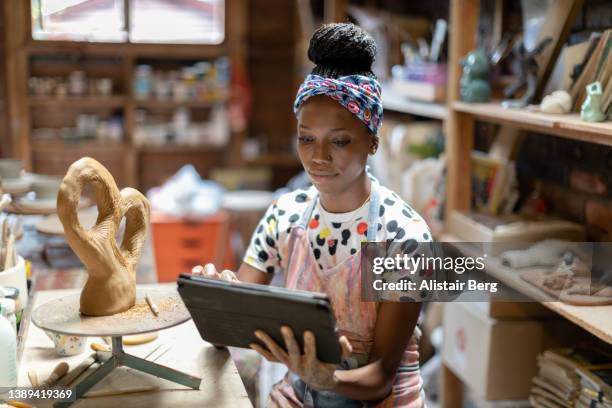 female sculptor using a digital tablet in her art studio - side hustle stock pictures, royalty-free photos & images