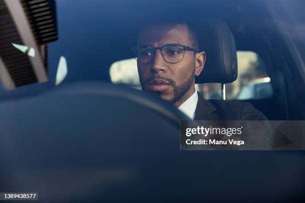 man dressed in a suit driving his vehicle to work in the morning, looking straight ahead with a serious expression. - man car stock pictures, royalty-free photos & images