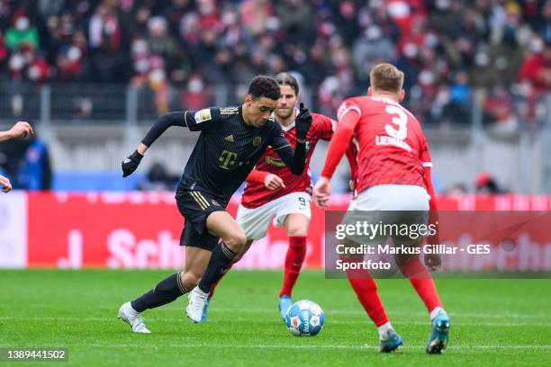Jamal Musiala of Munich challenges for the ball with Lucas Hoeler and Philipp Lienhart of Freiburg during the Bundesliga match between Sport-Club...