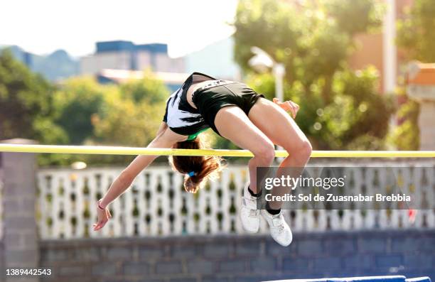 close up of a teenage girl practicing high jump passing backwards with good technique over the bar on a beautiful sunny day - hochsprung stock-fotos und bilder